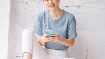 Joyful redhead young woman wearing wireless earphones listening relaxed music using cell phone.