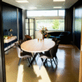 Uitzicht door een deuropening op een luxe vergader- of loungeruimte met een ovale houten tafel, fluwelen stoelen en een donkerblauwe bank, met uitzicht op een groen landschap.
