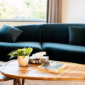 Close-up van een comfortabele zithoek met een donkergroene fluwelen bank en een ovale houten salontafel met een plant en tijdschriften.
